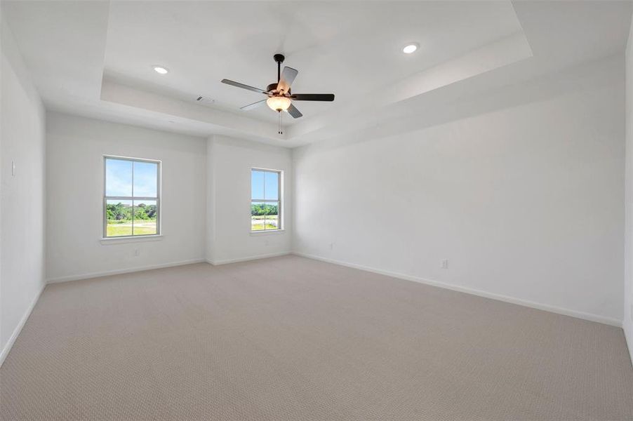 Spacious interior room featuring a tray ceiling with recessed lighting and a ceiling fan Spacious interior room featuring a tray ceiling with recessed lighting and a ceiling fan