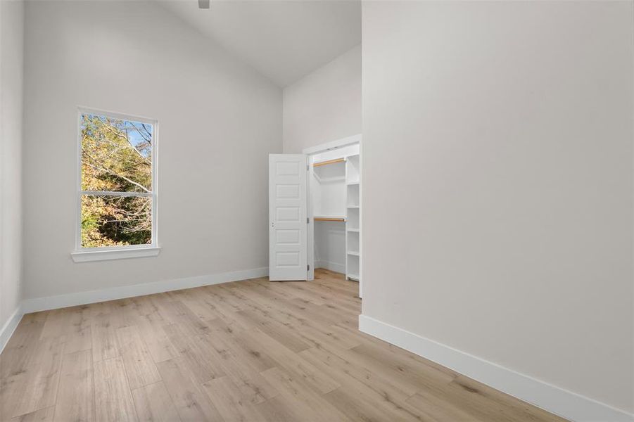 Unfurnished bedroom featuring light wood-type flooring and high vaulted ceiling