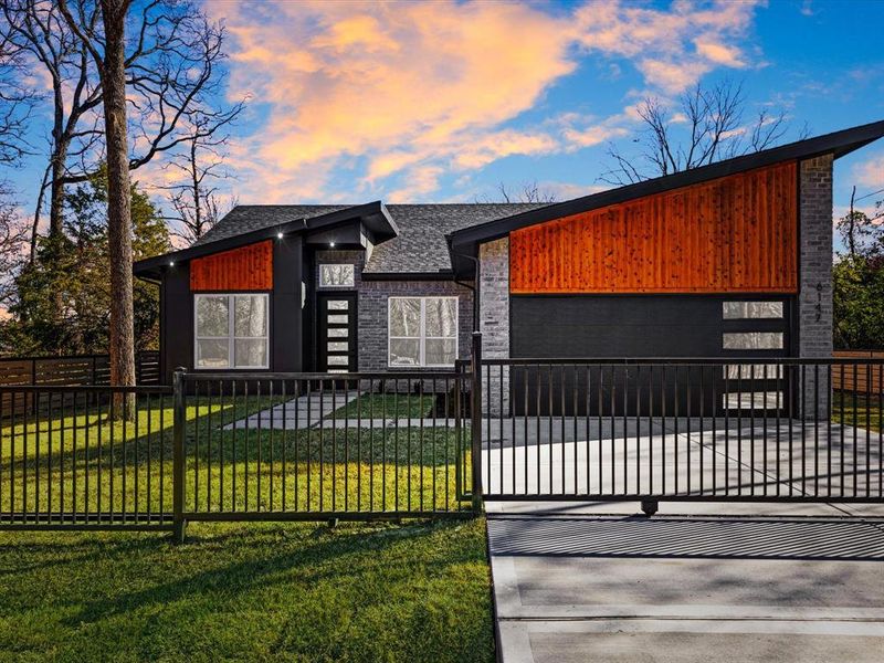 Contemporary home featuring a garage, driveway, a fenced front yard, a shingled roof, and a gate