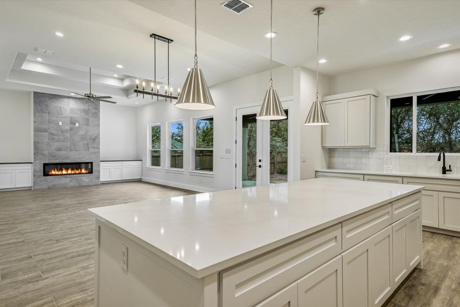 Kitchen featuring a fireplace, light wood-style floors, white cabinetry, a ceiling fan, and a tray ceiling