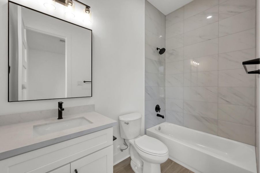 Beautifully finished secondary bathroom featuring a modern vanity with quartz countertops, designer lighting, and a full tub/shower with large-format tile surround.