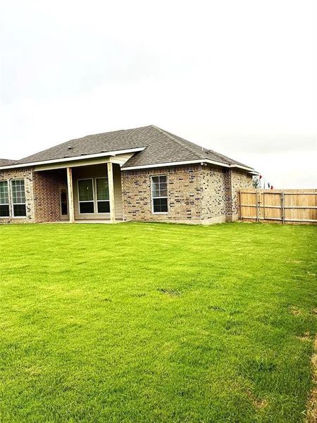 Expansive green lawn with a covered patio, brick exterior, multiple windows, and a wood privacy fence Expansive green lawn with a covered patio, brick exterior, multiple windows, and a wood privacy fence