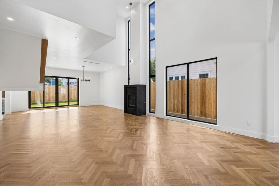 Expansive living area with soaring ceilings, herringbone wood floors, and abundant natural light from large windows and sliding doors. Expansive living area with soaring ceilings, herringbone wood floors, and abundant natural light from large windows and sliding doors.