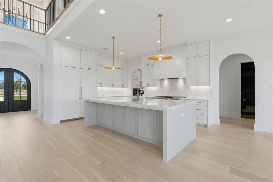 Gourmet kitchen featuring a large central island with light-toned cabinetry and a light-toned countertop, a range with a matching backsplash and custom hood, and recessed lighting