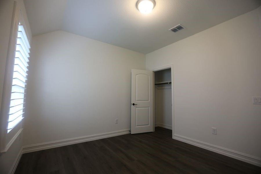 Room featuring wood-finish flooring, white baseboards, a window with plantation shutters, an arched panel door, and a built-in closet with hanging rod