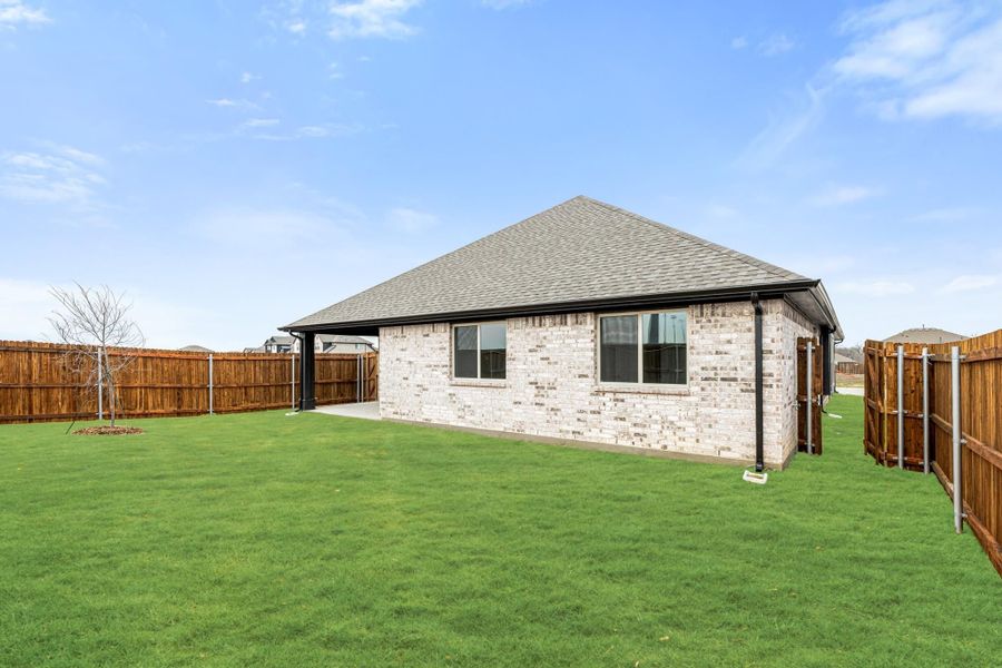 Backyard of single-story brick home with green lawn, wood privacy fence, and gray shingle roof