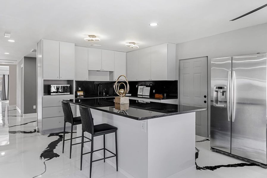 Kitchen with stainless steel appliances, a kitchen bar, a center island, white cabinets, and dark stone countertops
