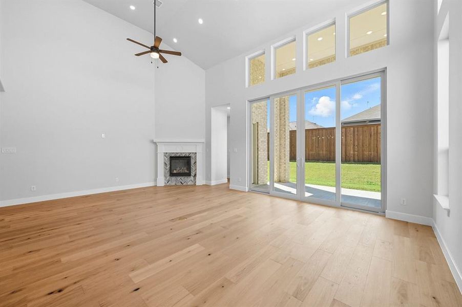 Unfurnished living room with a towering ceiling, a premium fireplace, light wood-style floors, a ceiling fan, and recessed lighting