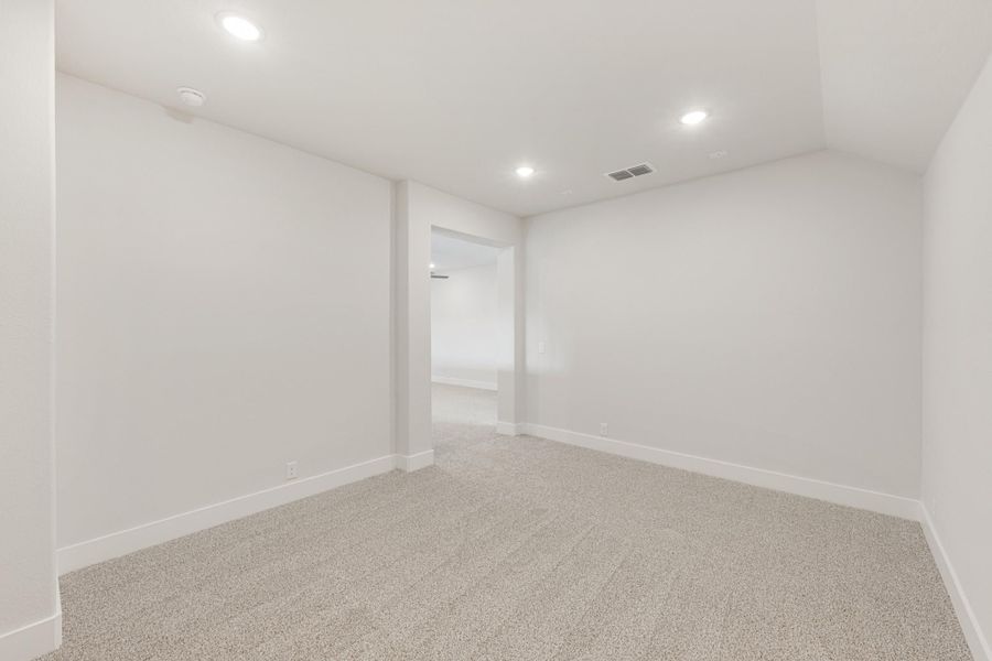 Empty room with white walls, carpet flooring, recessed lighting, and an open doorway leading to another room.