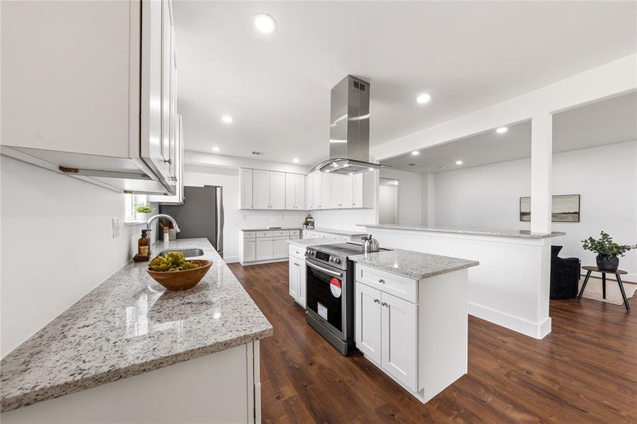 Modern kitchen featuring white cabinetry, light-toned countertops, a stainless steel range hood, and wood-finish flooring