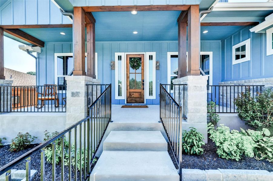 Inviting front entrance featuring a wood-panel door with sidelights, a covered porch with exposed wood beams, stone-clad pillars, and wrought iron railings