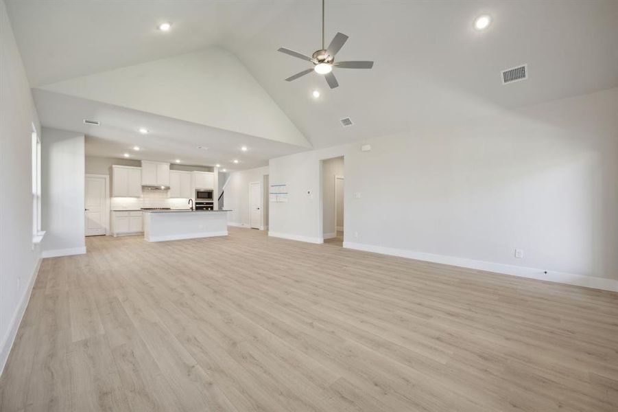 Unfurnished living room with light wood-type flooring, high vaulted ceiling, ceiling fan, and sink