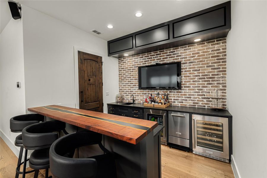 Bar featuring butcher block counters, sink, light hardwood / wood-style flooring, brick wall, and beverage cooler