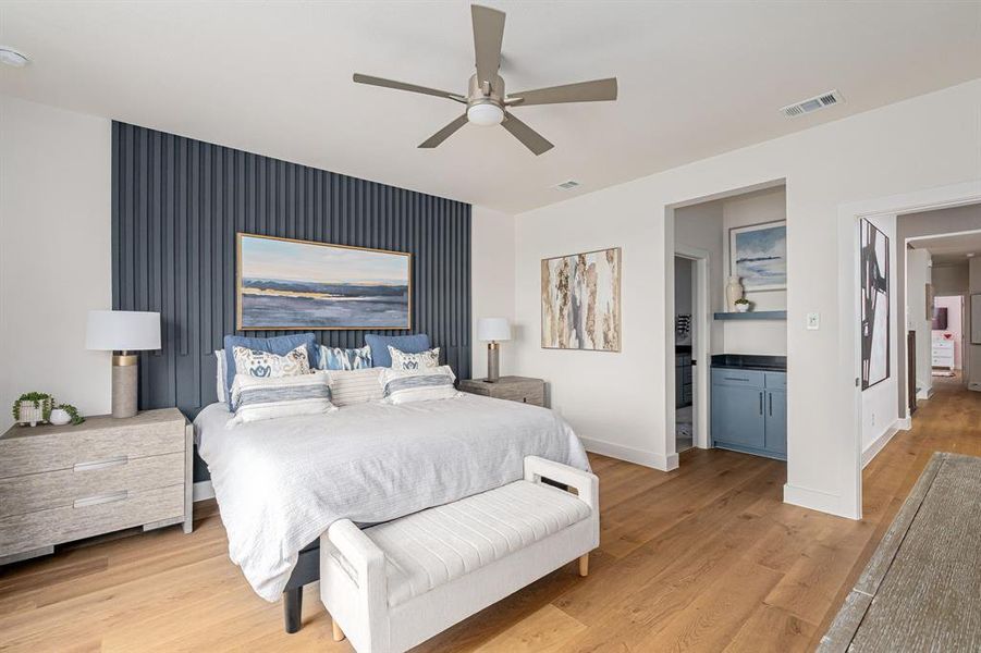 Bedroom with light wood finished floors, ceiling fan, and an accent wall