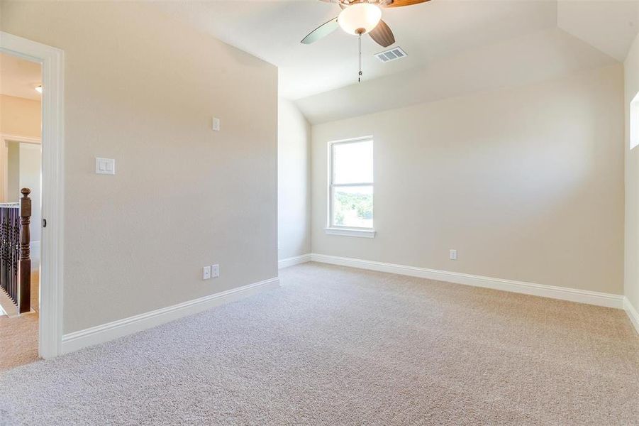 Empty room featuring ceiling fan, vaulted ceiling, and light colored carpet