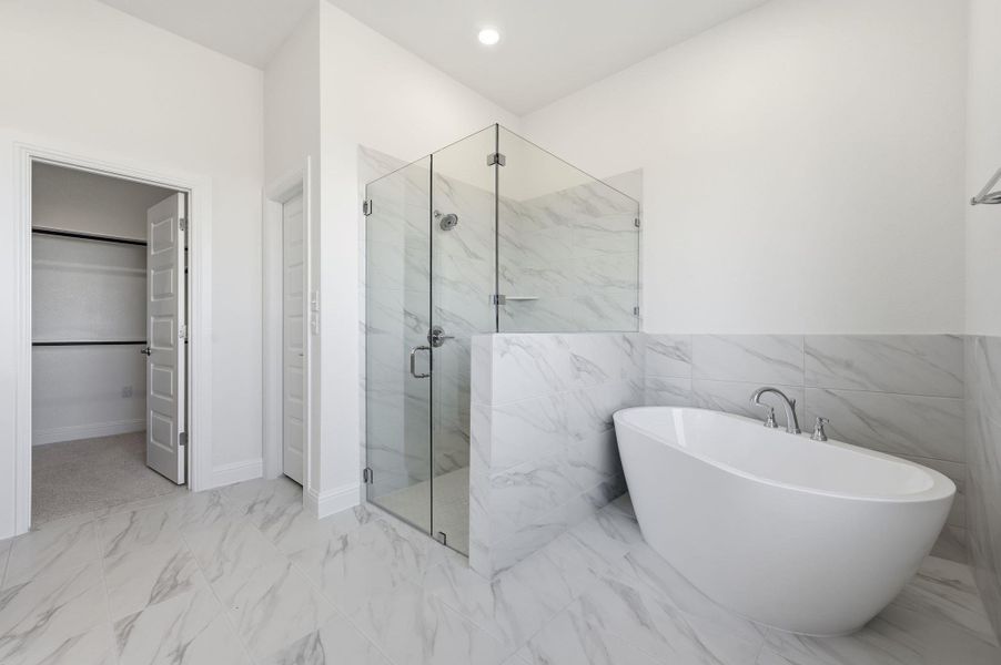 Full bath with a walk in closet, a freestanding bath, a marble finish shower, light marble finish flooring, and tile walls