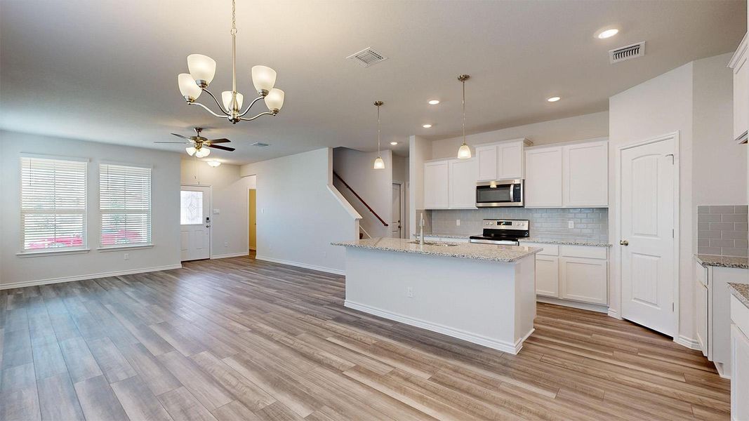 Kitchen with a center island with sink, open floor plan, hanging lights, white cabinetry, and light stone countertops