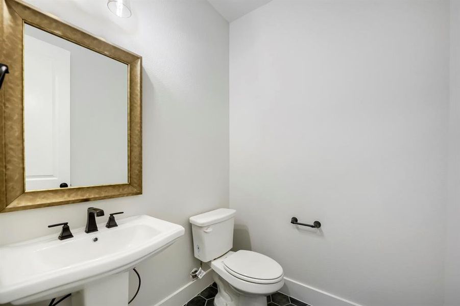 Pedestal sink with matte black faucet, framed mirror, and hexagonal tile flooring