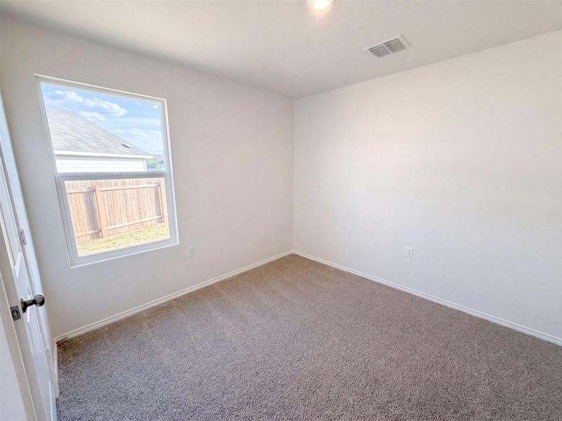 Soft carpeting pairs with neutral walls and a window overlooking the backyard fence.