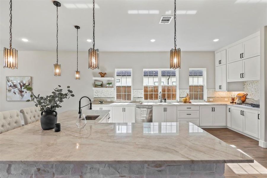 Kitchen with white cabinets, pendant lighting, a kitchen bar, a spacious island, and light stone countertops Kitchen with white cabinets, pendant lighting, a kitchen bar, a spacious island, and light stone countertops