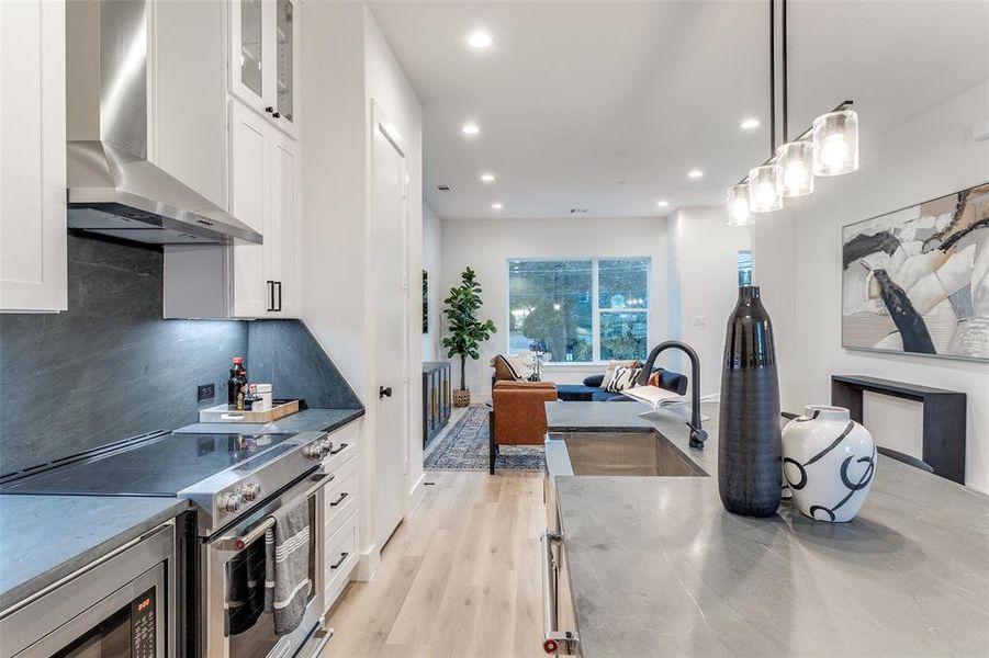 Kitchen with sink, white cabinets, wall chimney range hood, stainless steel appliances, and decorative light fixtures