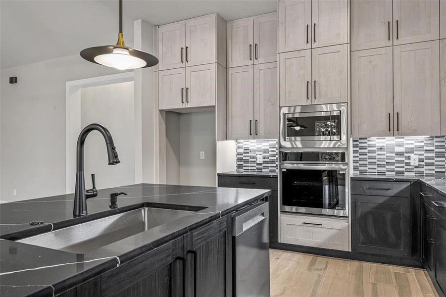 Kitchen with stainless steel appliances, light hardwood / wood-style floors, backsplash, dark stone counters, and sink