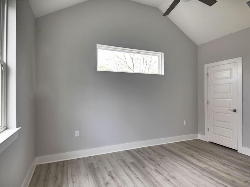 Empty room featuring light wood-style flooring, lofted ceiling, and a ceiling fan
