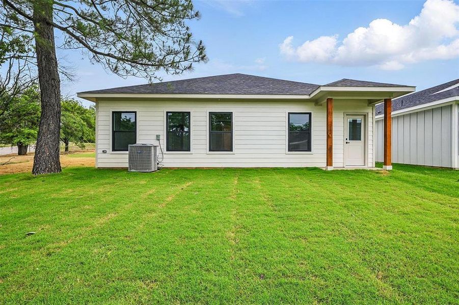Rear view of house with a yard, central AC unit, and roof with shingles