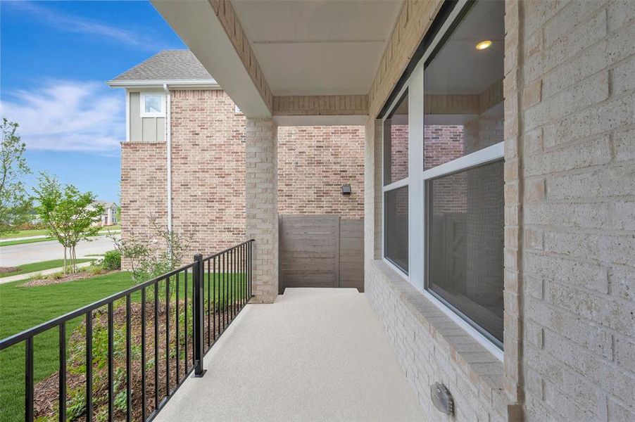 Covered front porch featuring a textured concrete surface, black metal railing, and light-colored brick exterior