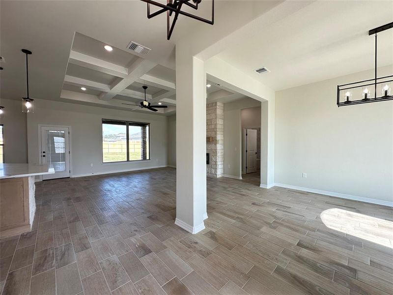 Unfurnished living room featuring a chandelier, coffered ceiling, beam ceiling, a fireplace, and wood finish floors
