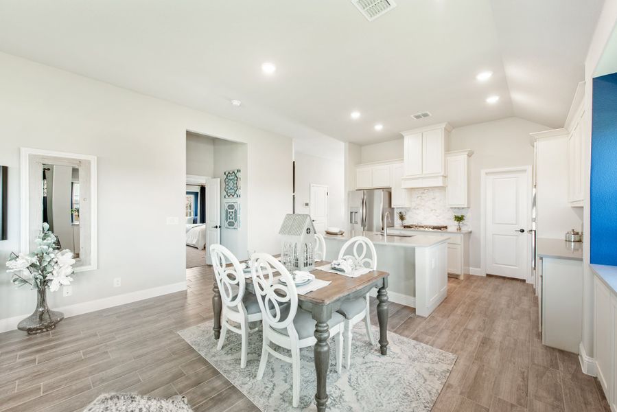 Open dining area with wood table and white chairs, connected to kitchen with white cabinets and island, hardwood floors throughout