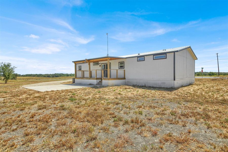 A spacious front porch overlooks the expansive surrounding fields under clear blue skies.