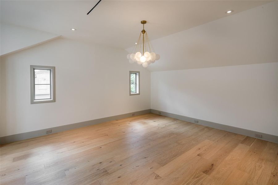 The primary suite keeps things beautifully restrained. Wide-plank oak floors, a sculptural chandelier, and a vaulted ceiling create a room that feels expansive without trying too hard.