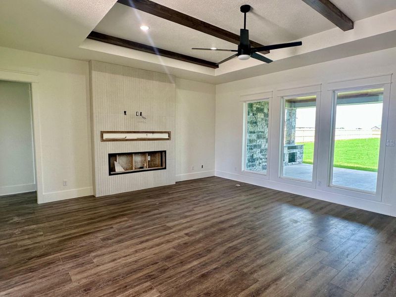 Unfurnished living room featuring ceiling fan, dark wood-style flooring, a fireplace, a textured ceiling, and a tray ceiling