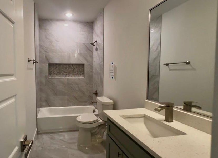 Full bathroom with a tub/shower combination, featuring large format tile surrounds and a decorative mosaic niche
