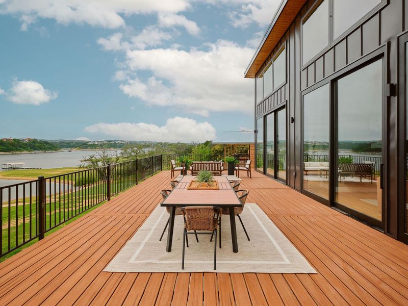 Expansive outdoor deck featuring wood-finish flooring, a black metal railing, and extensive glass doors