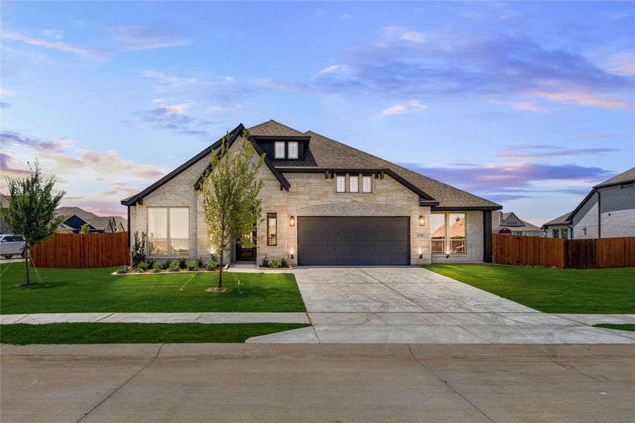 Single-story home with stone exterior, two-car garage, and manicured front lawn at dusk