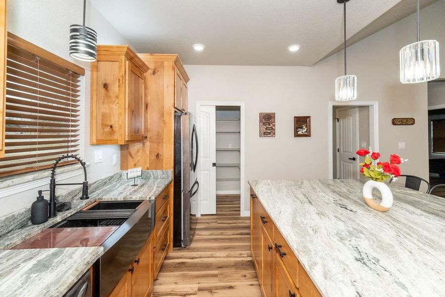 Kitchen featuring stainless steel fridge, light stone countertops, hanging light fixtures, and light hardwood / wood-style flooring