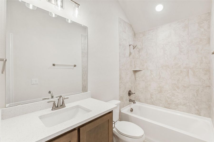 Bathroom with single-sink vanity, quartz countertop, tiled shower-tub combo, and large mirror