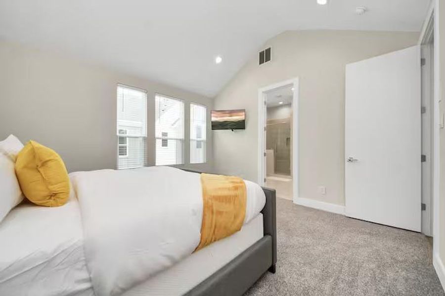 The primary suite feels noticeably open thanks to its vaulted ceiling, multiple windows, and direct connection to the private bath.