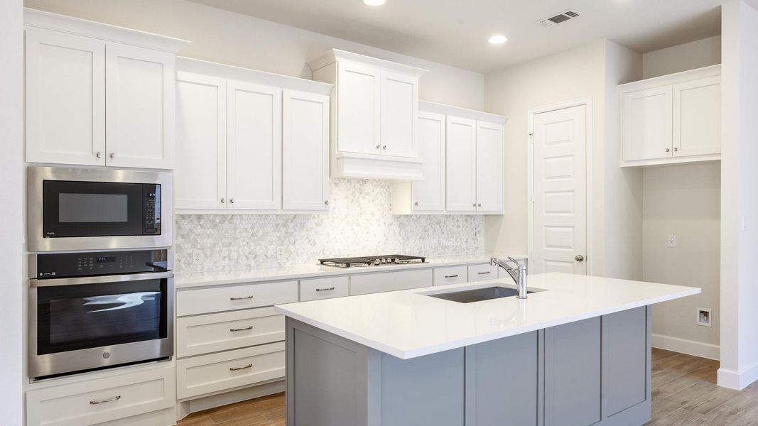 Kitchen with white cabinetry, appliances with stainless steel finishes, gray cabinetry, backsplash, and a center island with sink Kitchen with white cabinetry, appliances with stainless steel finishes, gray cabinetry, backsplash, and a center island with sink