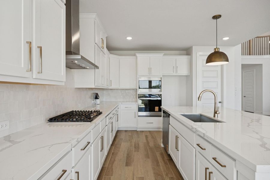 The kitchen showcases modern white cabinetry accented with gold-toned hardware, a coordinating subway tile backsplash and stainless steel appliances, including a built-in oven.