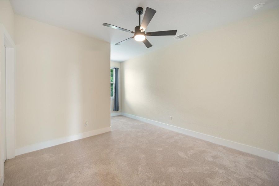 A quiet retreat with plush carpeting and a modern ceiling fan, offering a serene atmosphere.