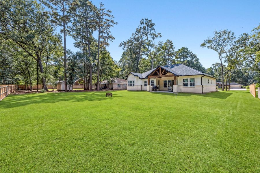 BACKYARD — Expansive backyard provides abundant green space surrounded by mature trees, offering a peaceful backdrop with room to enjoy the outdoors.