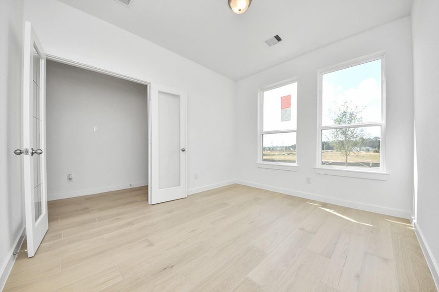 Experience the perfect blend of sophistication and warmth in this home office, boasting elegant wood-look tile flooring and flooded with natural light from expansive windows and French doors. Sample photo of completed home with similar floor plan. Actual colors and selections may vary.