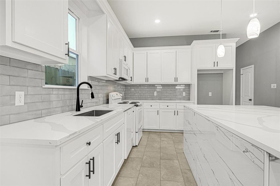 This modern kitchen features sleek white cabinetry, marble countertops, and a stylish gray subway tile backsplash. It includes a spacious island with pendant lighting and ample storage, creating a bright and inviting space perfect for cooking and entertaining.