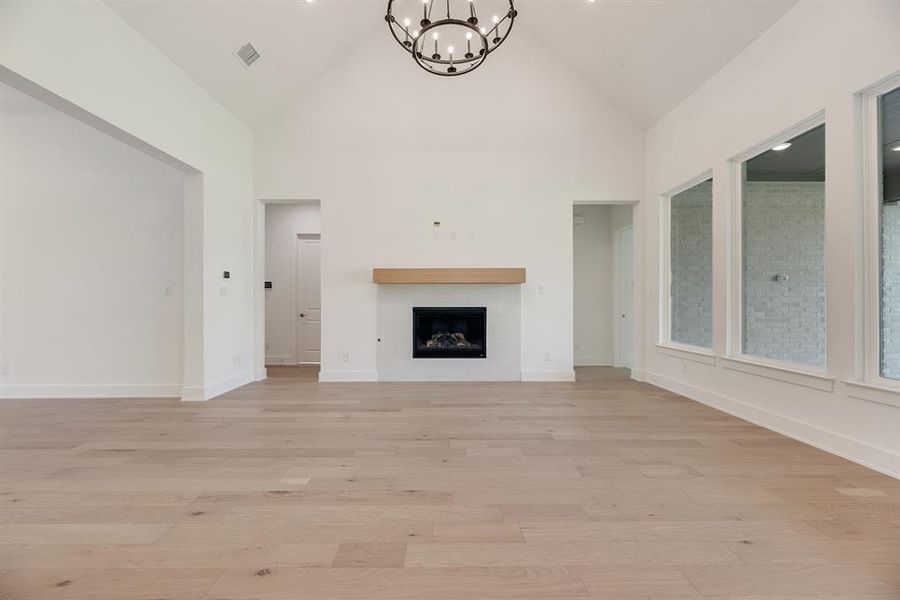 Unfurnished living room featuring high vaulted ceiling, a fireplace, light wood-style flooring, and a chandelier