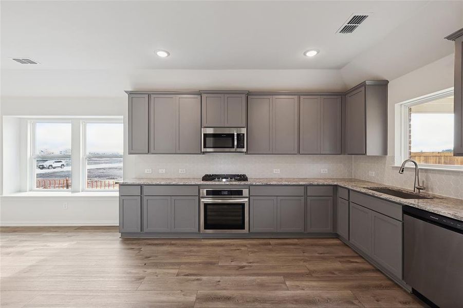 Kitchen featuring stainless steel appliances, gray cabinets, tasteful backsplash, light stone countertops, and recessed lighting