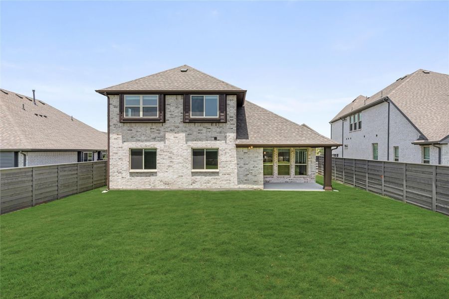 Two-story brick home rear view with covered patio, large green lawn, and wood privacy fence Two-story brick home rear view with covered patio, large green lawn, and wood privacy fence