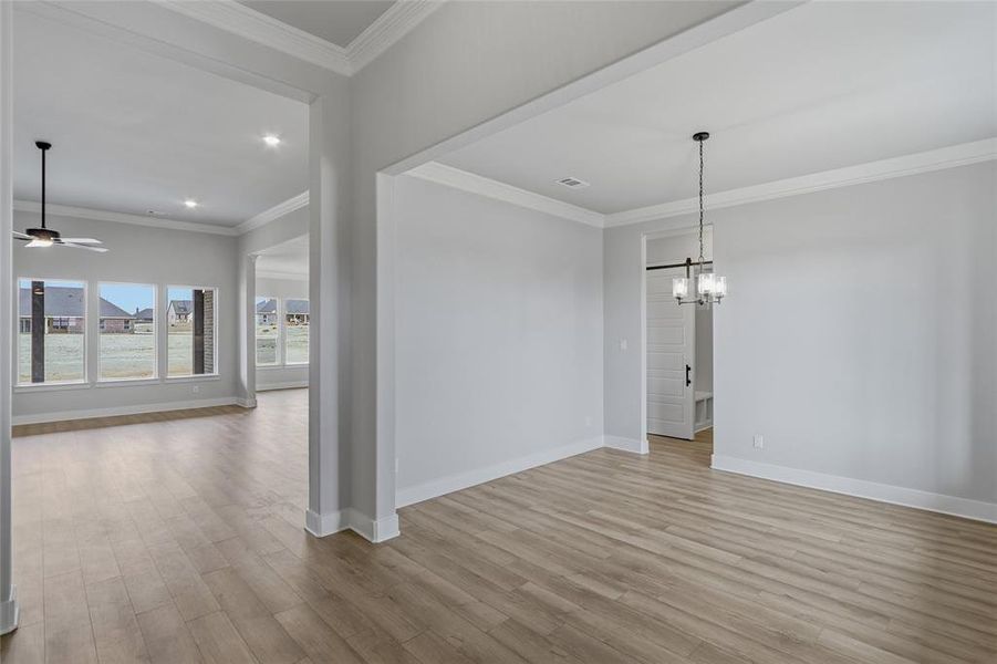 Unfurnished dining area featuring crown molding, light wood finished floors, ceiling fan, and suspended lighting